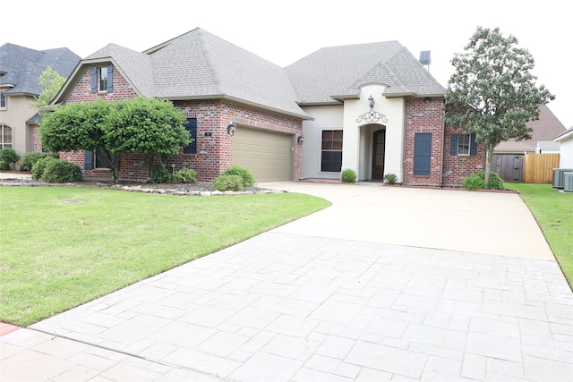 french provincial home featuring a front yard, a garage, and central air condition unit