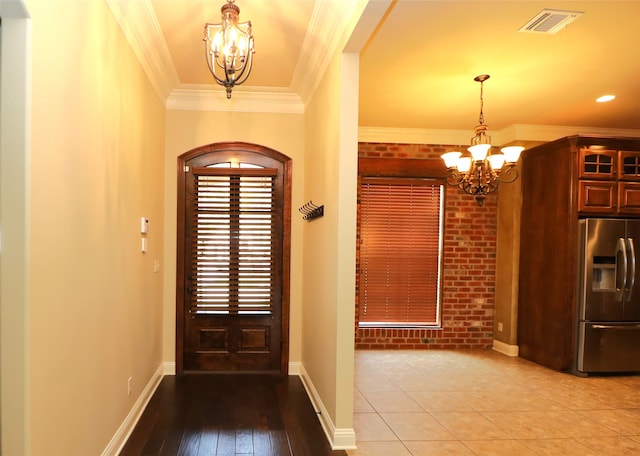 foyer entrance featuring wood-type flooring, brick wall, a notable chandelier, and ornamental molding