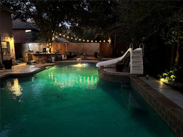 pool at twilight with a patio area, a diving board, and a water slide