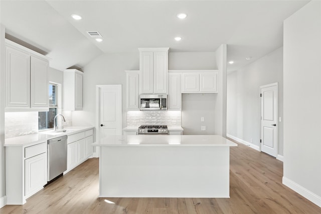 kitchen featuring white cabinets, stainless steel appliances, vaulted ceiling, and a kitchen island