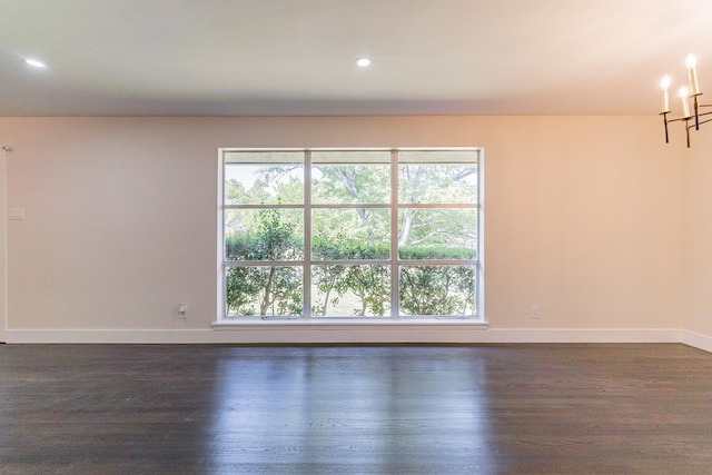 spare room featuring an inviting chandelier and dark hardwood / wood-style floors