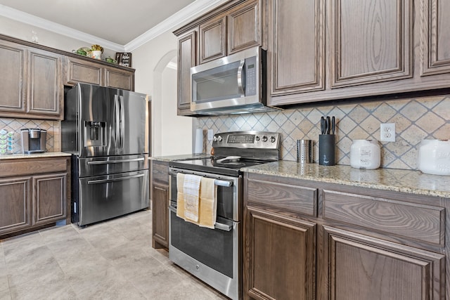 kitchen with light stone counters, stainless steel appliances, tasteful backsplash, ornamental molding, and dark brown cabinets