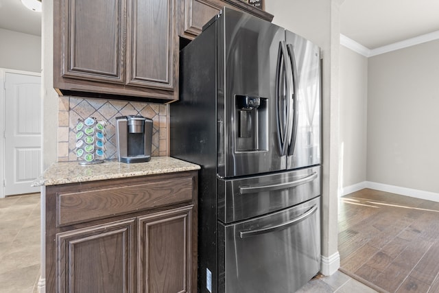 kitchen with light stone counters, light wood-type flooring, dark brown cabinetry, and stainless steel fridge