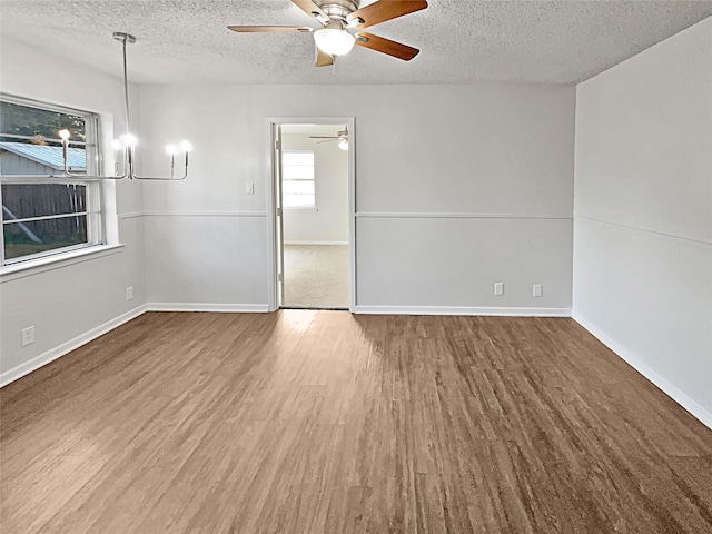 empty room featuring ceiling fan with notable chandelier, hardwood / wood-style floors, and a textured ceiling