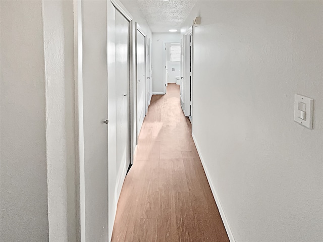 hallway with a textured ceiling and light hardwood / wood-style floors