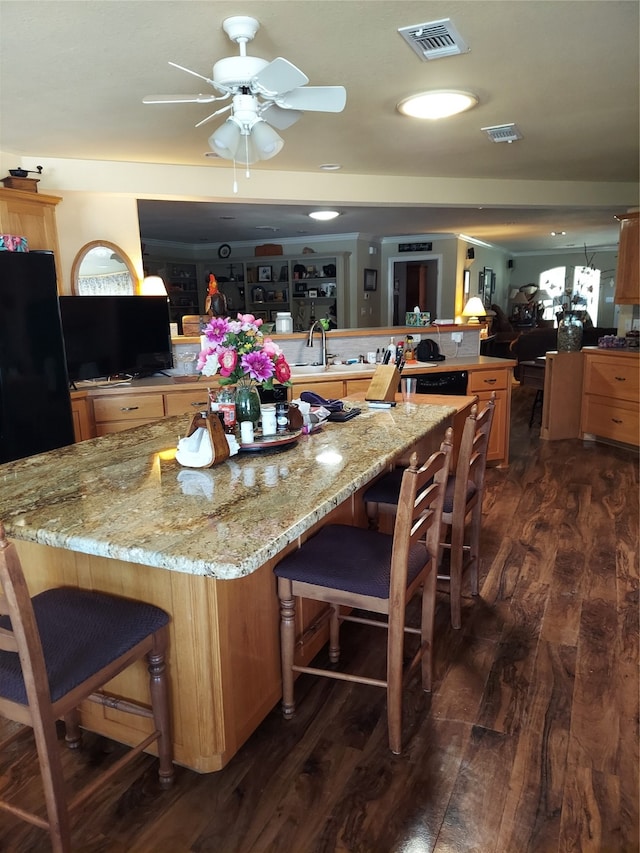 kitchen with a large island with sink, a kitchen breakfast bar, kitchen peninsula, light stone counters, and dark hardwood / wood-style flooring