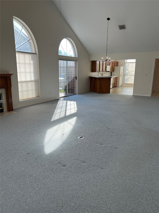 unfurnished living room featuring a notable chandelier, light carpet, and high vaulted ceiling