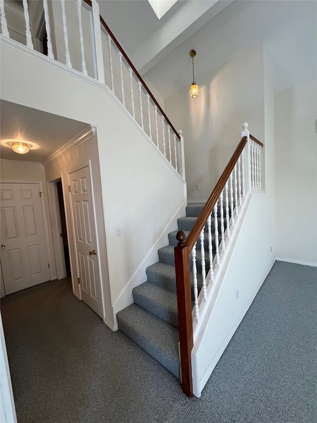 stairs with a towering ceiling, crown molding, and carpet