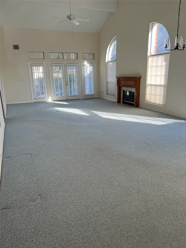 unfurnished living room featuring ceiling fan with notable chandelier, carpet flooring, high vaulted ceiling, and a healthy amount of sunlight