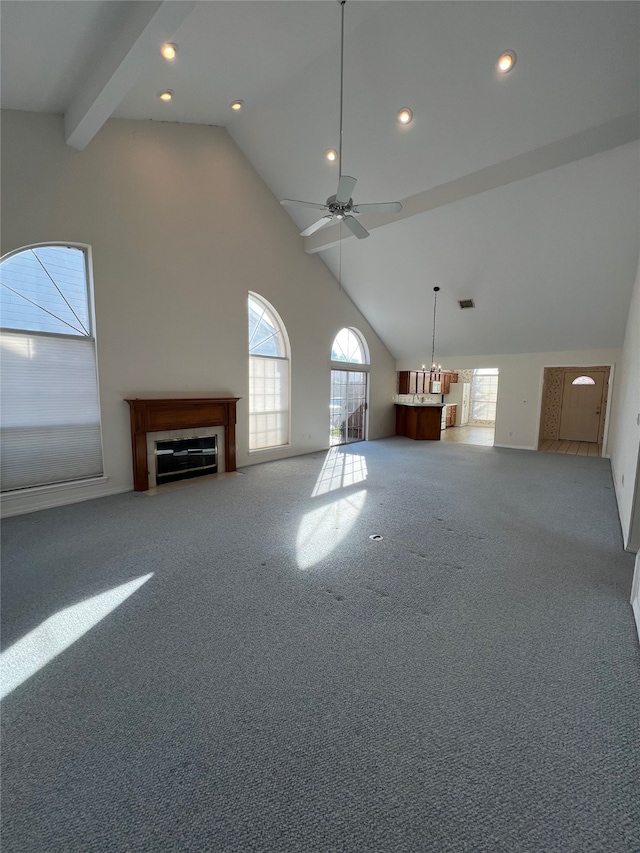 unfurnished living room with carpet floors, ceiling fan, beam ceiling, a fireplace, and high vaulted ceiling