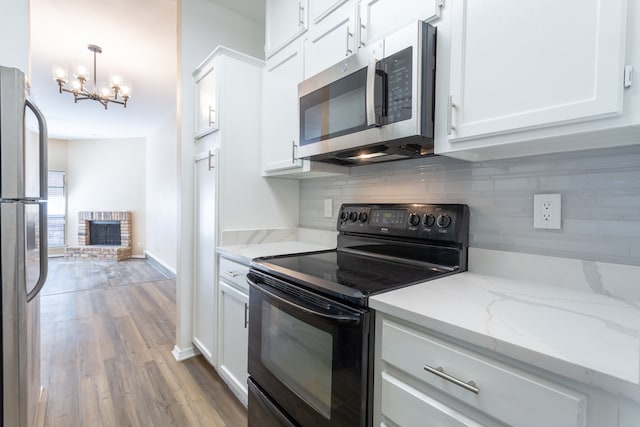 kitchen featuring stainless steel appliances, a brick fireplace, decorative light fixtures, white cabinets, and light hardwood / wood-style floors