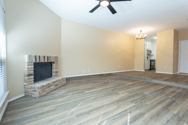 unfurnished living room featuring ceiling fan with notable chandelier, light wood-type flooring, and a brick fireplace