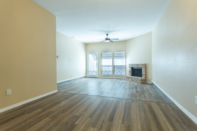 unfurnished living room featuring a brick fireplace, dark hardwood / wood-style floors, and ceiling fan