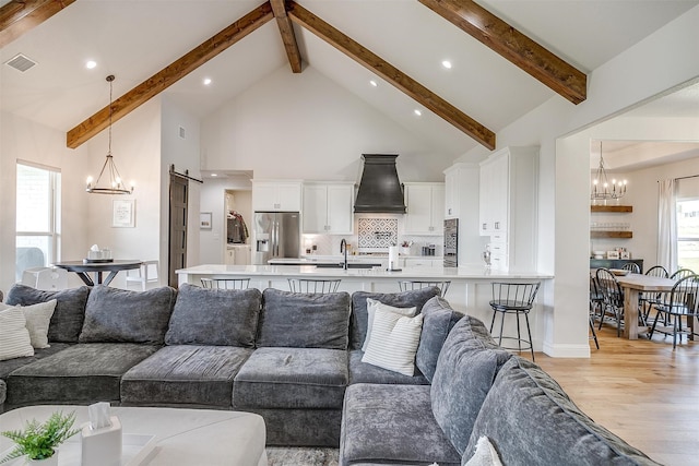 living room with a barn door, light hardwood / wood-style floors, high vaulted ceiling, and beam ceiling