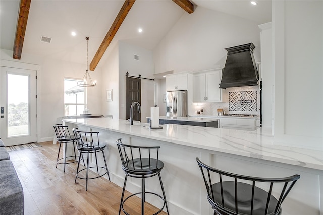 kitchen with beamed ceiling, light hardwood / wood-style floors, a barn door, a breakfast bar area, and appliances with stainless steel finishes