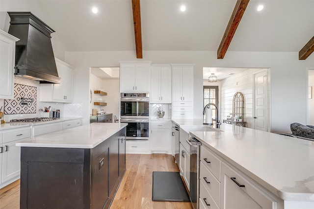 kitchen featuring a center island with sink, beamed ceiling, and appliances with stainless steel finishes