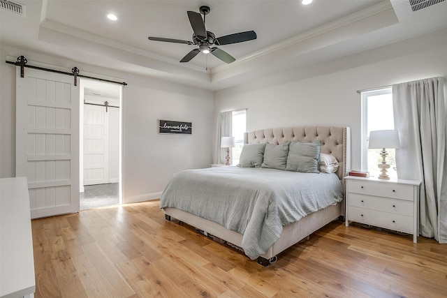 bedroom featuring ceiling fan, ornamental molding, wood-type flooring, a tray ceiling, and a barn door