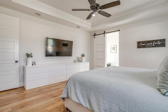 bedroom with ceiling fan, a tray ceiling, a barn door, light hardwood / wood-style flooring, and ornamental molding