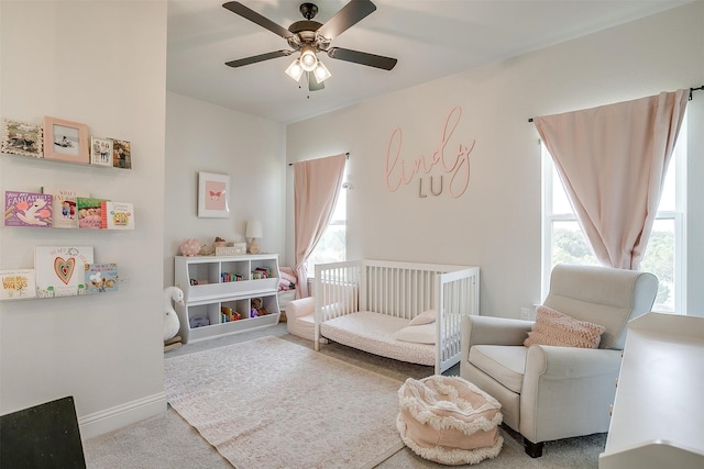 bedroom with ceiling fan, a nursery area, and light carpet