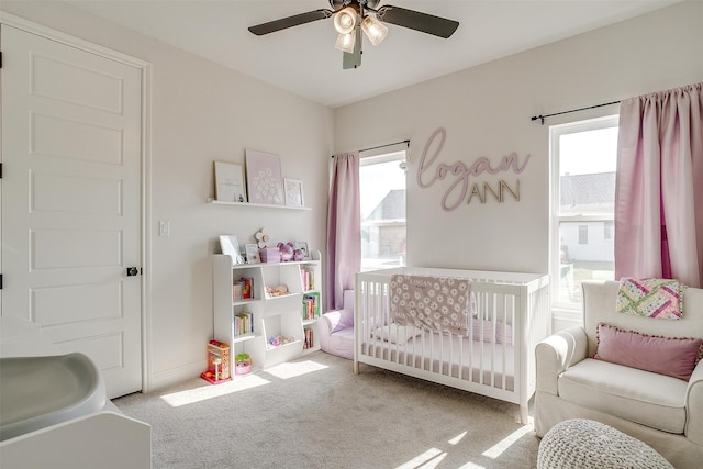 bedroom featuring a crib, light colored carpet, multiple windows, and ceiling fan