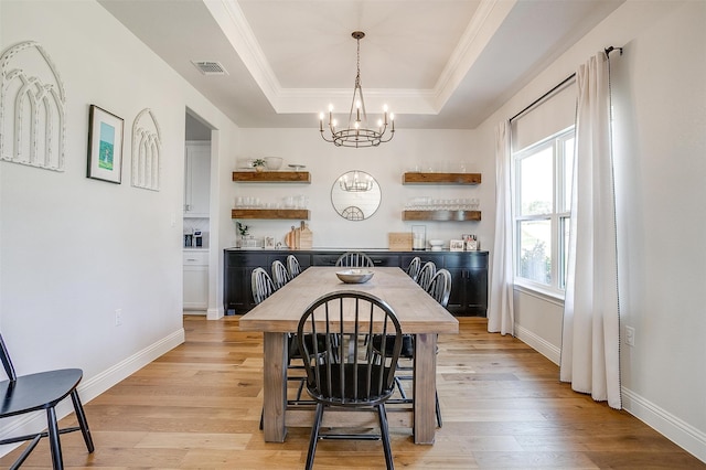 dining space with ornamental molding, a chandelier, a raised ceiling, and light hardwood / wood-style flooring