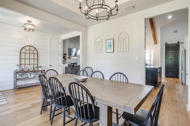 dining space featuring light hardwood / wood-style flooring, wood walls, a barn door, and lofted ceiling