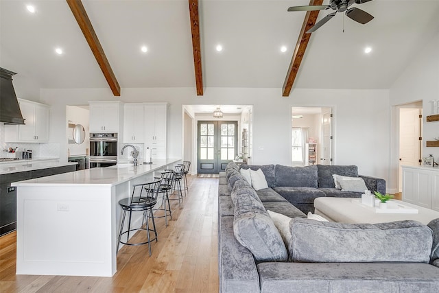 living room with beamed ceiling, light wood-type flooring, ceiling fan, french doors, and high vaulted ceiling