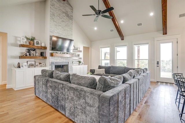 living room featuring high vaulted ceiling, beam ceiling, a stone fireplace, and light hardwood / wood-style flooring