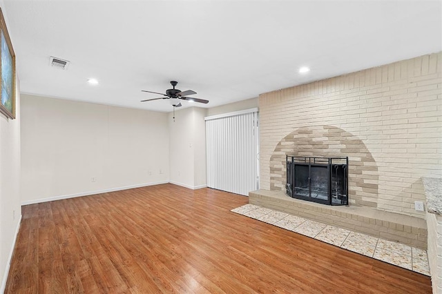 unfurnished living room featuring wood-type flooring, a brick fireplace, and ceiling fan