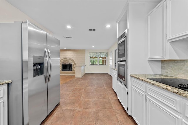 kitchen with a brick fireplace, decorative backsplash, light stone counters, white cabinetry, and stainless steel appliances