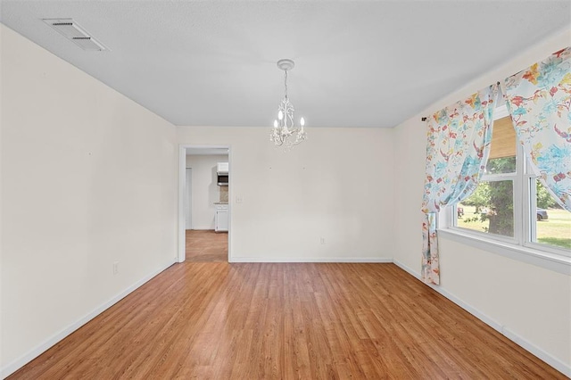 spare room featuring wood-type flooring and a notable chandelier