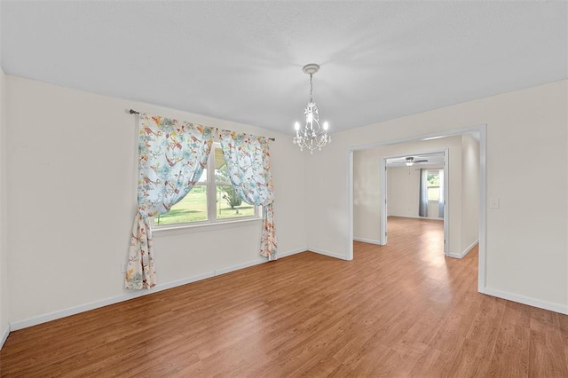 spare room featuring light wood-type flooring, a wealth of natural light, and a chandelier