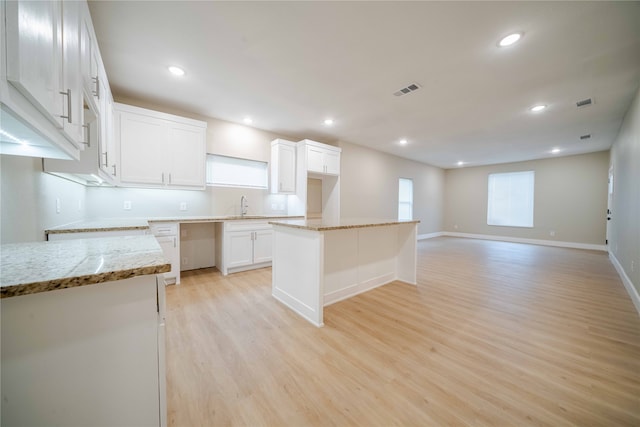 kitchen with white cabinetry, sink, light stone countertops, a center island, and light wood-type flooring