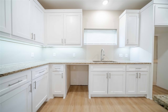 kitchen featuring light stone countertops, light hardwood / wood-style floors, white cabinetry, and sink