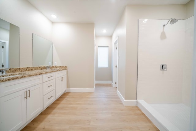 bathroom featuring wood-type flooring, a tile shower, and vanity