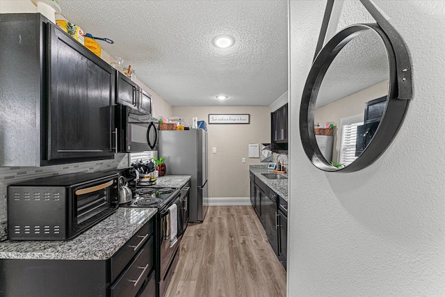 kitchen with light stone countertops, light wood-type flooring, a textured ceiling, stainless steel appliances, and sink