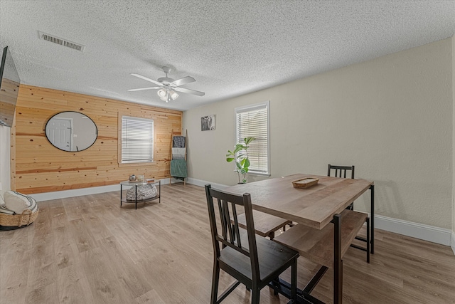 dining room featuring a textured ceiling, light hardwood / wood-style flooring, ceiling fan, and wooden walls