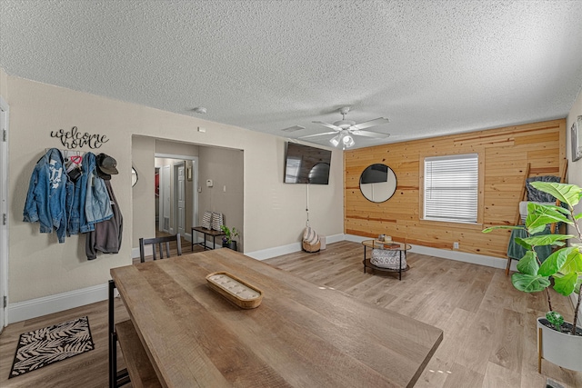 dining space with wooden walls, ceiling fan, a textured ceiling, and light wood-type flooring