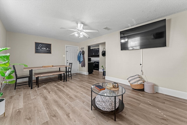 living room with a textured ceiling, light hardwood / wood-style flooring, and ceiling fan