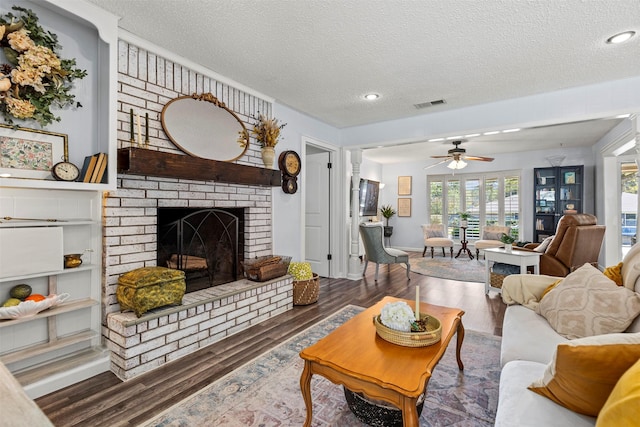 living room featuring ceiling fan, wood-type flooring, a textured ceiling, and a brick fireplace