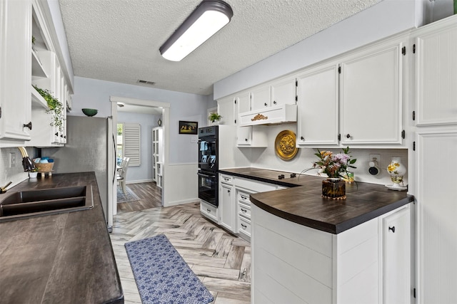 kitchen featuring light parquet floors, white cabinets, black appliances, and a textured ceiling