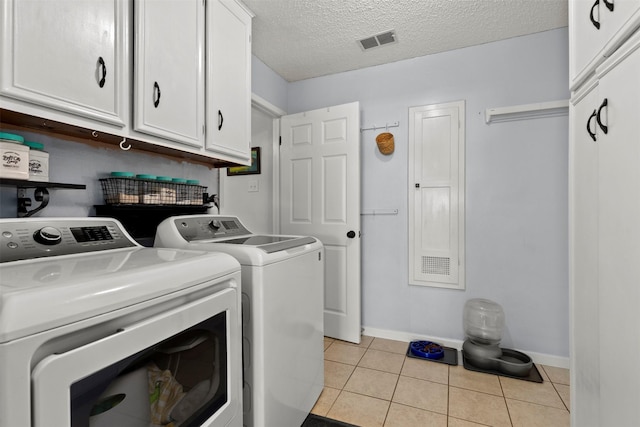 clothes washing area with separate washer and dryer, light tile patterned floors, cabinets, and a textured ceiling