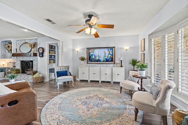 living room featuring a textured ceiling, ceiling fan, dark hardwood / wood-style flooring, and a fireplace