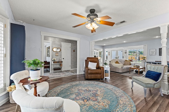 living room featuring dark hardwood / wood-style floors, ceiling fan, ornate columns, and a textured ceiling