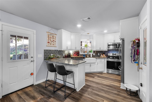 kitchen with white cabinetry, stainless steel appliances, a kitchen breakfast bar, kitchen peninsula, and dark stone countertops