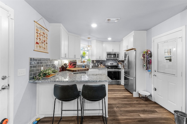 kitchen featuring stainless steel appliances, a kitchen breakfast bar, kitchen peninsula, decorative backsplash, and white cabinets