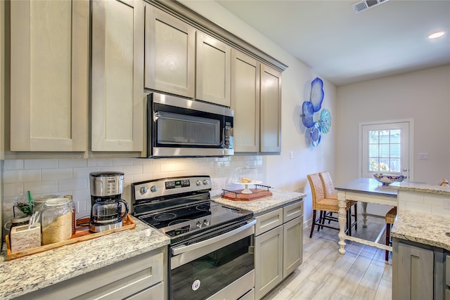 kitchen featuring gray cabinets, tasteful backsplash, light hardwood / wood-style flooring, light stone countertops, and appliances with stainless steel finishes