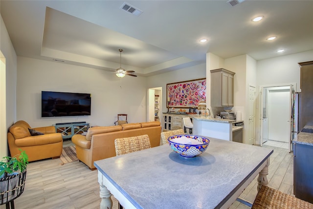 dining room featuring light wood-type flooring, ceiling fan, sink, and a raised ceiling