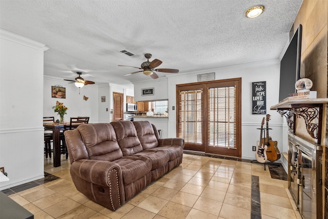 living room featuring ceiling fan, crown molding, light tile patterned floors, and a textured ceiling