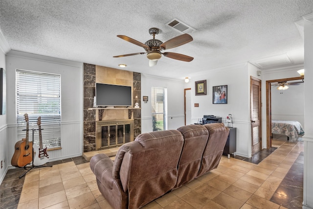 living room featuring a fireplace, ceiling fan, ornamental molding, and a textured ceiling